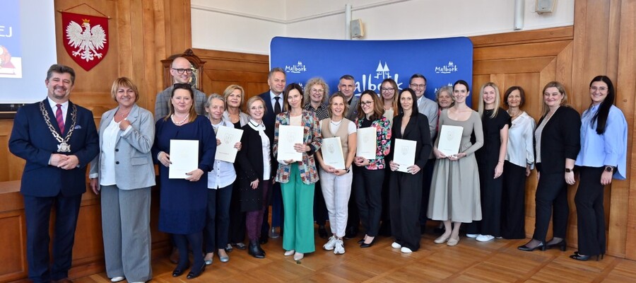 wspóne zdjęcie nagrodzonych nauczycieli, dyrektorów i przedstawicieli miasta na ściance z napisem Malbork