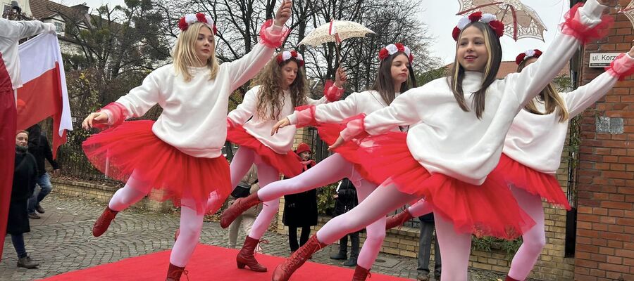 dziewczynki w biało-czerwonych strojach tańczą na scenie z parasolkami