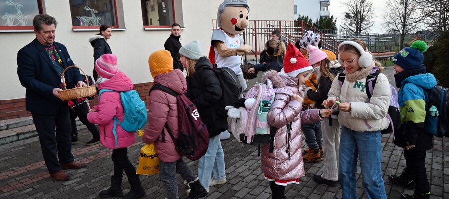 burmistrz i Marianek rozdają uczniom upominki przed szkołą